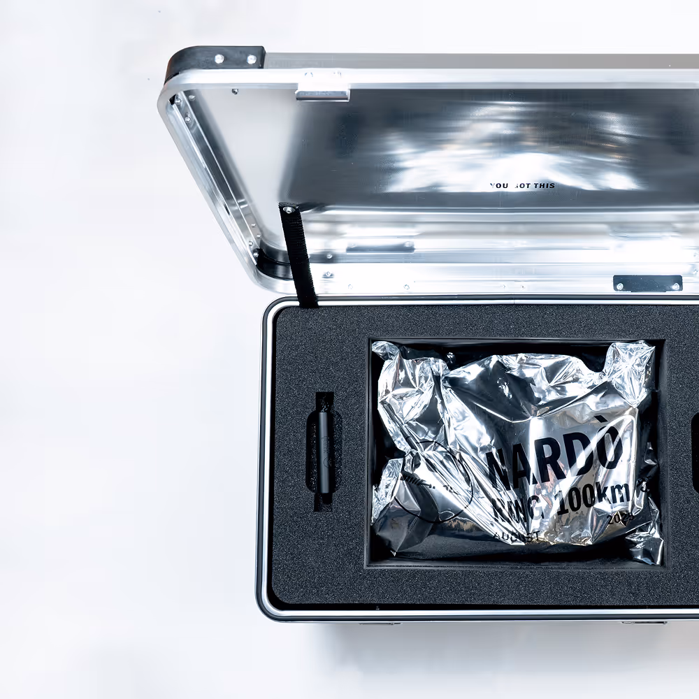 An open aluminium case revealing a foil-wrapped package stamped “NARDÒ RING 100KM”, part of the adidas Nardo campaign packaging